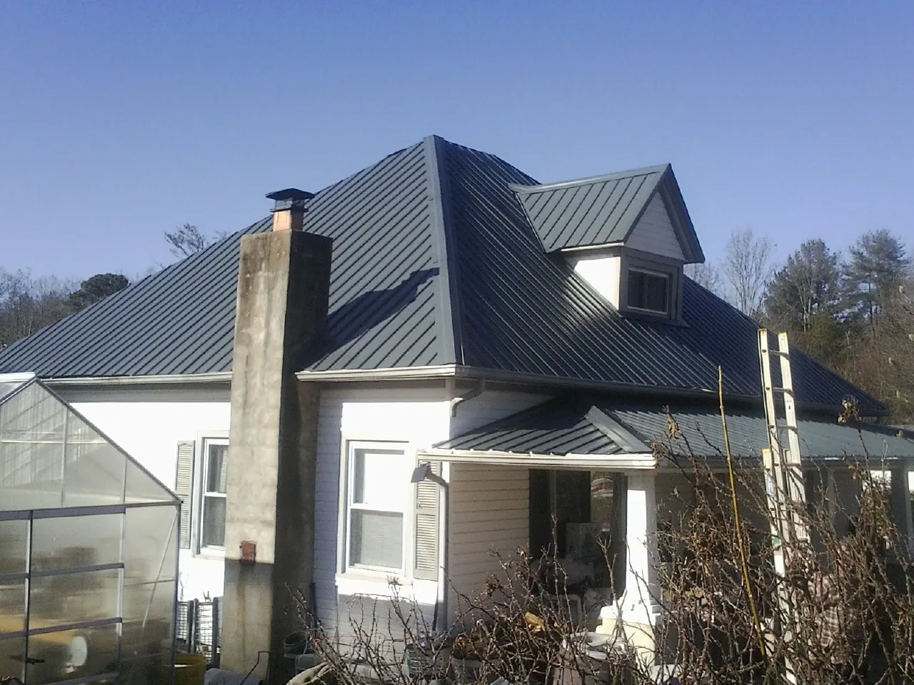 Dark blue standing seam metal roof on a white farmhouse with dormer — Slate & Tile Roof Repair by Roofing Brothers in Broadbent