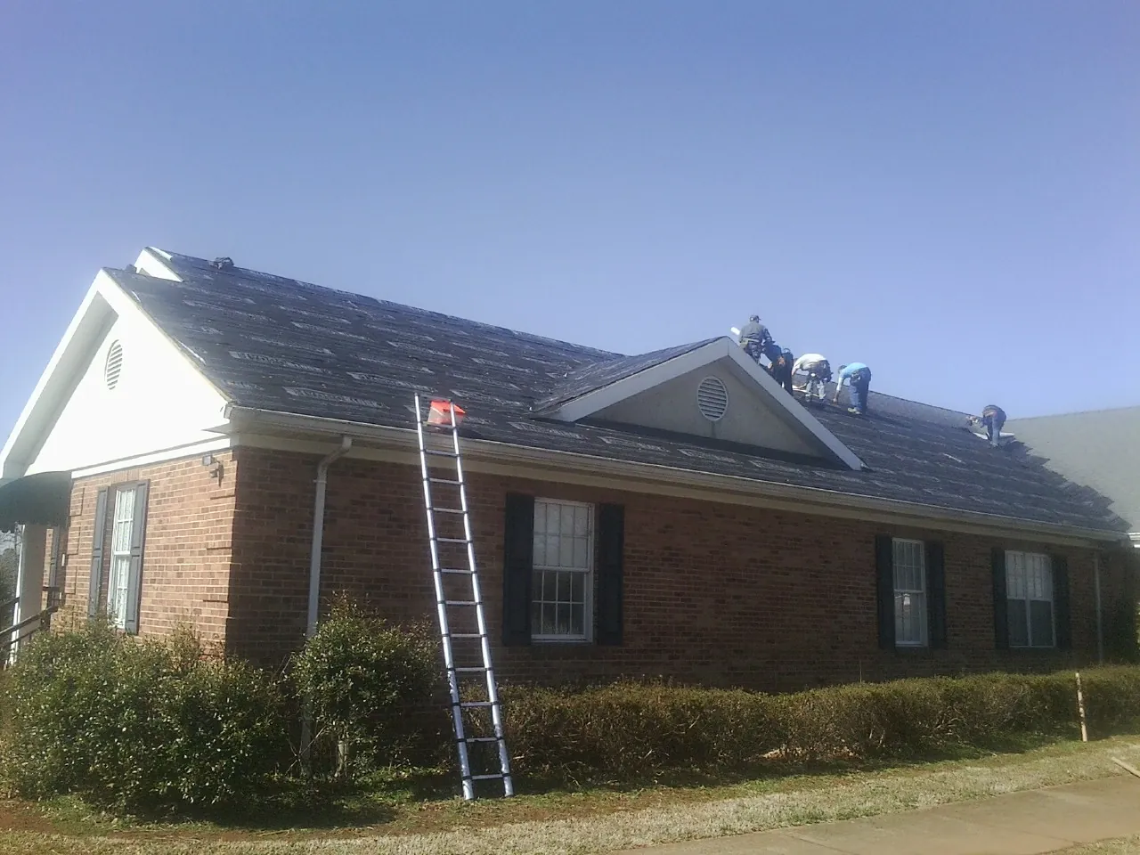 Crew tearing shingles off a brick ranch roof with a ladder set — Metal Roof Repair work by our crew in Broadbent