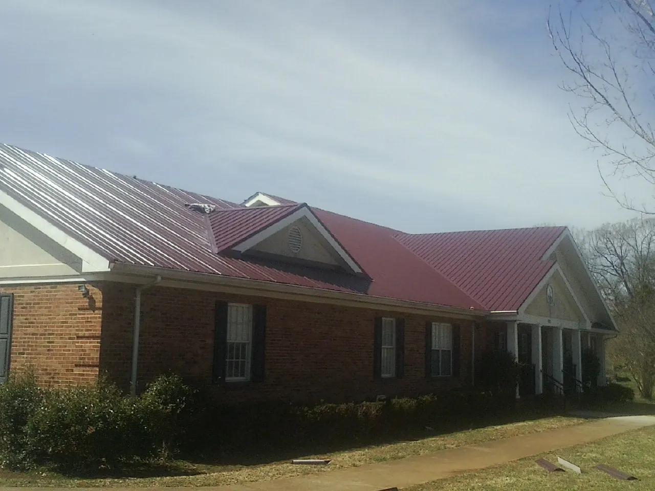 Red metal roof with gabled entries on a long brick building, from a Hail Damage Roof Repair job in Broadbent