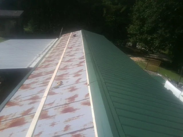 Old rusted panels beside newly installed green metal roofing — Wind Damage Roof Repair by Roofing Brothers in Broadbent