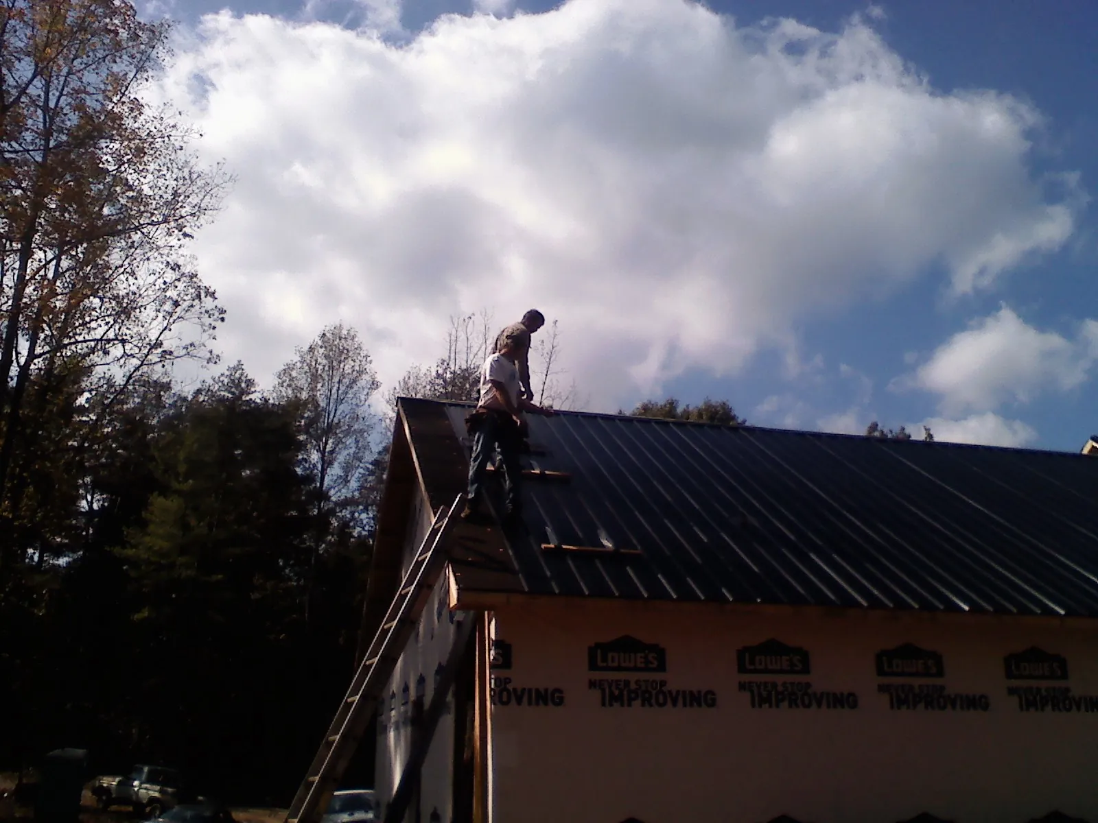 Roofer fastening dark metal panels high against a cloudy sky, from a Roof Inspection job in Broadbent
